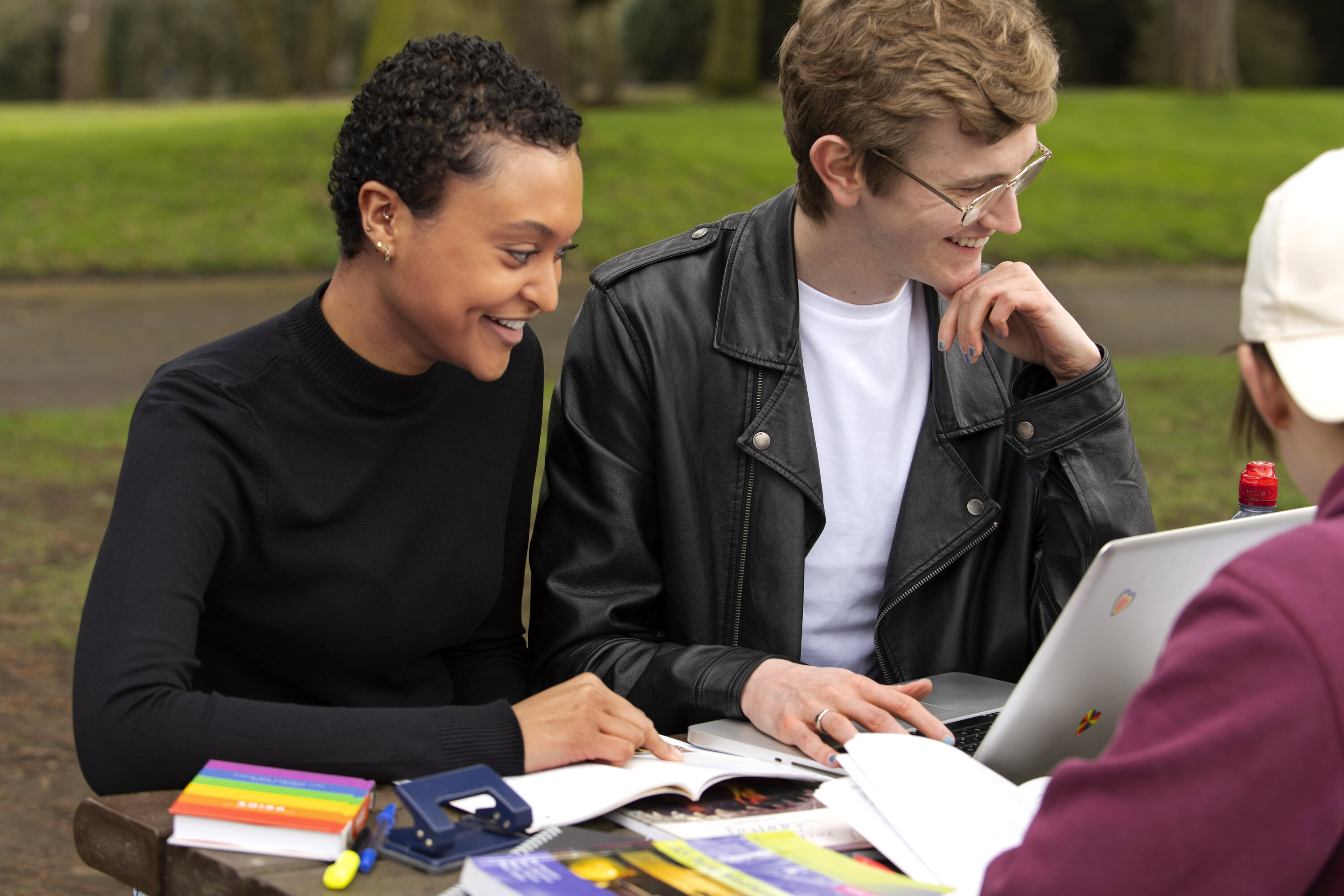 A group of young people sitting on a bench outside studying